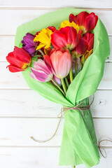 Bouquet of colorful tulips wrapped with green paper on white wooden  background 