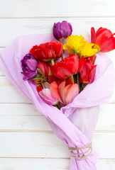 Bouquet of colorful tulips wrapped with pink paper on white wooden  background 