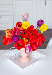Red and yellow tulips  bouquet in pink vase on a table in white kitchen