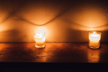 votive candles on wood shelf creating dramatic shadows on white brick wall - obrazy, fototapety, plakaty