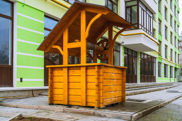 Obraz na płótnie Canvas An orange wooden well with a metal chain next to a new apartment building on a city street. Side view