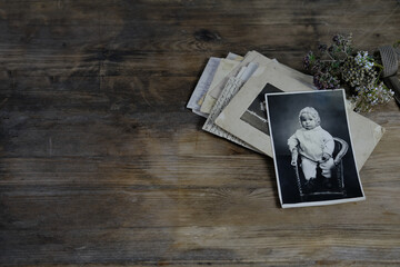 stack of retro monochrome photographs of 50-60s on natural wooden table, photo of child, dried flowers, concept of family tree, genealogy, connection with ancestors, memories of youth, childhood