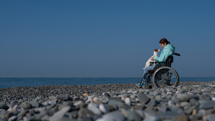 Fototapeta premium A serene Caucasian woman in a wheelchair is resting on the seashore with a jack russell terrier dog.