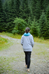 Child, teenager, girl dressed comfortably, and heading to the forest, walking through the forest, tall fir trees.