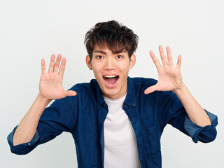 Portrait of handsome Chinese young man with curly black hair in blue shirt posing against white wall background. Hands open and shouting with big mouth, front view.