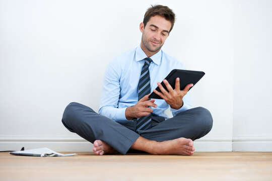 Keeping current after a day at work. A barefoot businessman sitting on the floor against a wall and using a digital tablet.