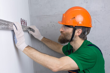 An electrician installs sockets in the apartment. A guy in an orange helmet and overalls makes electrics in the house.
