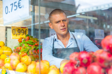 European supermarket worker setting out goods on showcase in greengrocer.