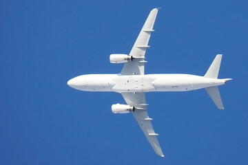 A white plane in flight on a blue sky background, bottom view