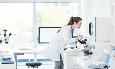 Observing and making notes. Cropped shot of a focused young female scientist conducting experiments...