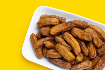 Sun-dried bananas in plate on yellow background.