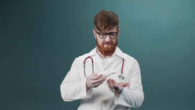 A man in a white medical gown cleans his hands with alcohol