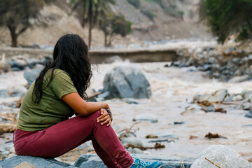 Woman sitting with her back to the bank of a mighty river.