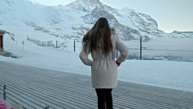 A fashionable girl in a winter jacket walking by The north face of the Eiger. A woman walks in slow motion in the winter in the Swiss Alps in  Kleine Scheidegg, Jungfrau Region, Switzerland.