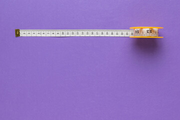 A coil with a measuring tape on a purple background. Flat lay. Place for text.