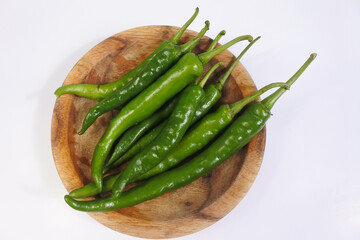 Some green chilies on a wooden plate on a white background