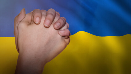 Pray for Ukraine message with a hand in prayer and the Ukrainian flag in the background.