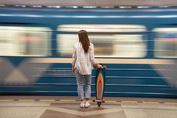 Woman wait for metro car at subway station with train passing by on background. Back rear view of...