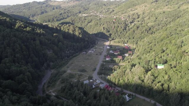 Aerial view, flying forward above a little romanian town between two green mountains covered in dense forest at daylight. 