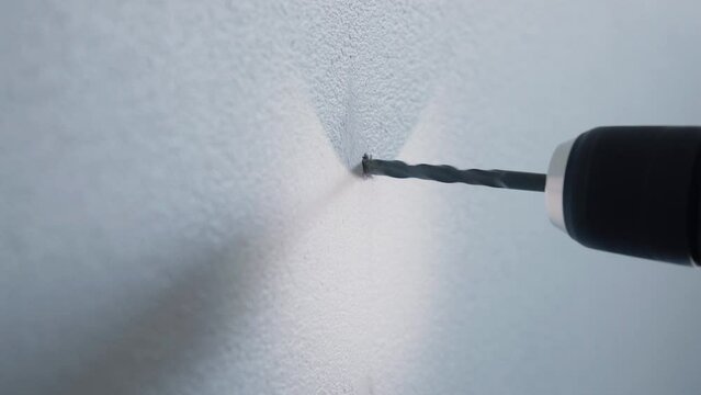 Young Male handyman using cordless screwdriver to mount a wooden magazine holder on a white wall with a srew at home detail close up  4K