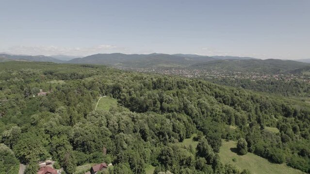 Ascending aerial view over dense forest landscape with houses far in the distance. Drone shot under clear sky without clouds. Romania.