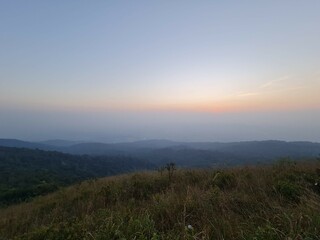 View from the top of the mountain, overlooking the grass on the ground stacked hills orange sky and a small sun