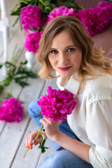 woman in shirt and jeans, holds bouquet of peonies in her hands, looks at camera and smiles. Portrait of beautiful blonde woman. Surprise bouquet of flowers for date, mothers day or valentines day