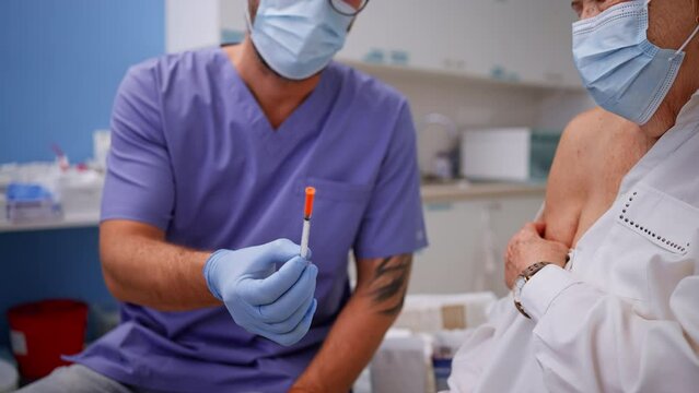 Doctor showing coronavirus vaccine to senior woman in his office.