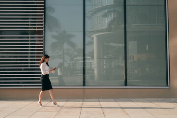 Obraz na płótnie Canvas Full length side portrait of a young woman walking and sending text message on cell phone