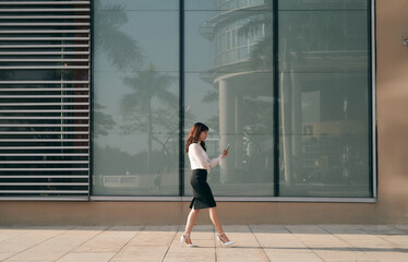 Full length side portrait of young woman walking on with cellphone