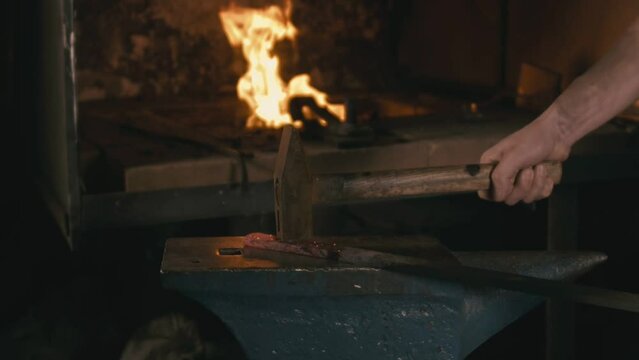 Forge workshop. Smithy manual production. Hands of smith with hammer hit on glowing hot metal, on the anvil, the forging process. Blacksmith makes iron products for manufacture of fireplace, stove.