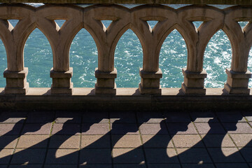Fototapeta premium A shadow falls on the pavement from patterned balusters. A flowing turquoise river can be seen in the background.