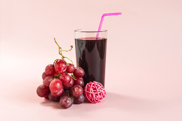 A bunch of grapes and a glass bottle with grape juice and colored decor on a pink background.