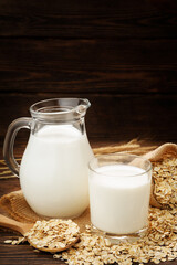 Oat flakes, jug and glass of milk on a wooden background.