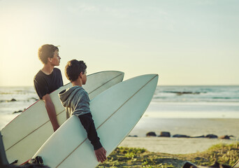 The waves are waiting. Shot of two young brothers holding their surfboards while looking towards...