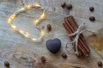 Chocolate heart, cinnamon, coffee beans and a glowing heart on a wooden background.