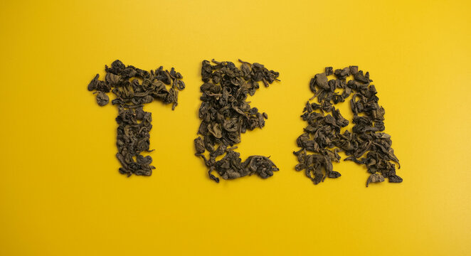 Word tea moving dried leaves brew. Flatlay on yellow background