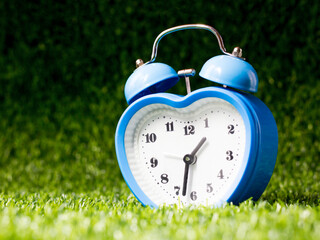 Blue alarm clock heart shape on the grass