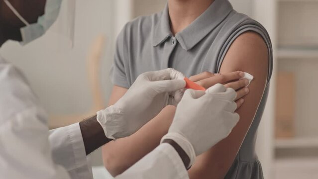 Cropped slowmo shot of unrecognizable little girl being vaccinated against Covid-19 by male doctor putting band aid on her shoulder after doing injection