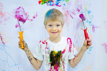 a small child boy stained and painted with paint holds a brush and a roller for drawing