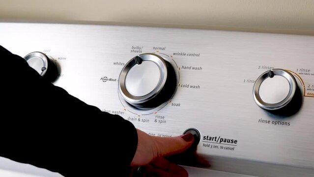 Hand turning the knobs for washing cycle, setting the temperature on the control panel, and pushing the start button of the electric clothes washing machine to begin laundry.