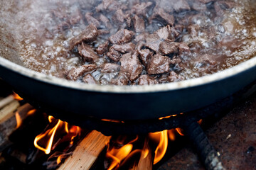 Pieces of meat for pilaf are stewed in cauldron over bonfire