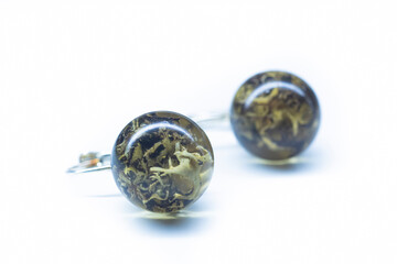 Dried moss earrings from epoxy resin. Natural withered plants preserved inside sphere handmade ball. Selective focus on the details, object isolated on white background.