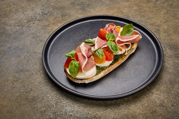 Close up bruschetta with mozzarella, Parma ham and pesto on black plate on textured background