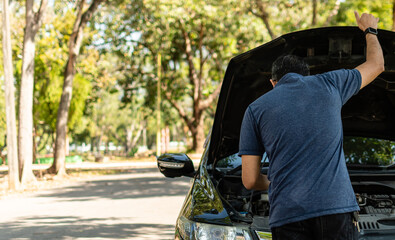 Man stands and inspects a broken-down car in a rural suburban forest. Black car, Engine won't start. Concept for roadside, damaged, stress, fix, problem. Close up, Selective focus, blurred background