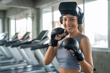 Portrait of Healthy Asian athletic woman in sportswear wearing VR glasses do boxing exercise workout in virtual reality cyberspace at fitness gym. Metaverse digital entertainment technology and sport