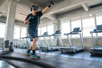 Naklejka na ściany i meble Healthy Asian athletic man in sportswear wearing VR glasses do punching boxing exercise workout in virtual reality cyberspace at fitness gym club. Metaverse digital entertainment technology and sport