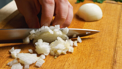 Close-up of a woman's hand with a knife on a cutting board, dicing onions.