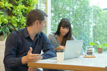 A relax happy latin young business couple talking in coffee shop or restaurant. People typing on computer laptop notebook device on social media internet technology. Lifestyle