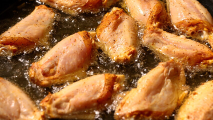 Chicken wings frying in a pan, close up shot. Poultry cooking at home, with hot oil bubbling in the skillet.